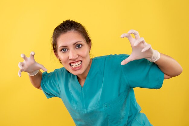 Médica vista frontal em luvas médicas com pose selvagem em fundo amarelo