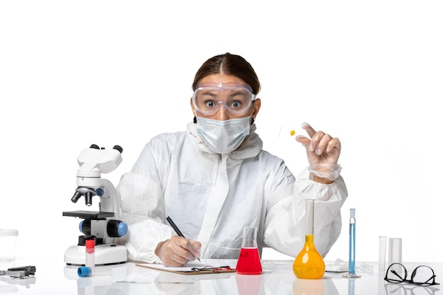Médica vista frontal em traje de proteção e com máscara escrevendo notas sobre fundo branco medicamento covid- vírus da pandemia de saúde