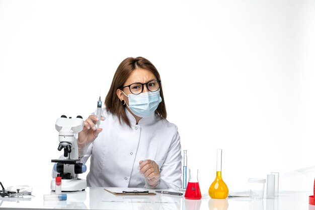 Médica vista frontal em traje médico branco com máscara devido a uma injeção secreta no espaço branco claro