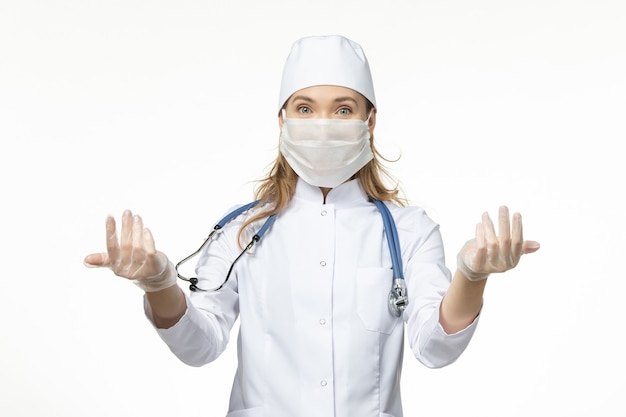 Médica vista frontal em traje médico com máscara estéril devido a coronavírus na pandemia de doença de mesa branca covid-