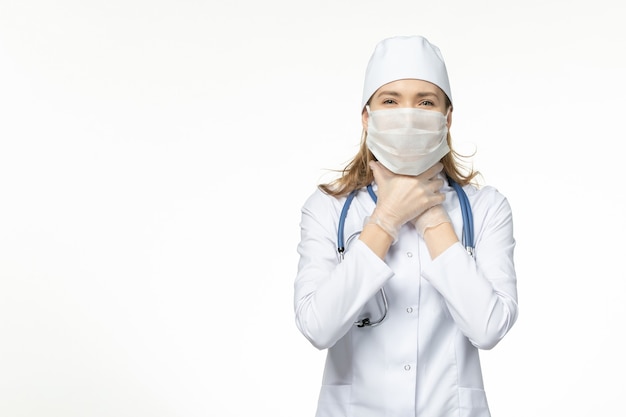 Médica vista frontal em traje médico usando máscara com luvas devido a coronavírus sofrendo de problemas respiratórios no vírus pandêmico da doença da mesa branca