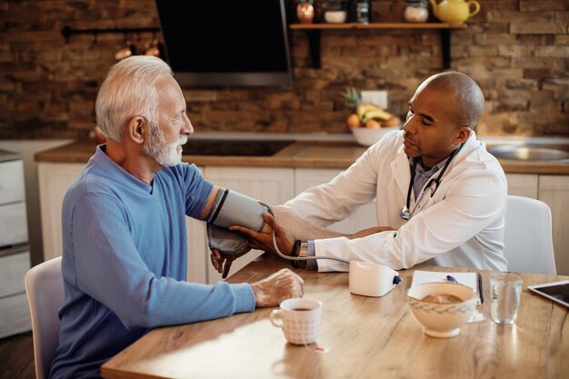 Médico afro-americano medindo a pressão arterial do homem sênior no lar de idosos