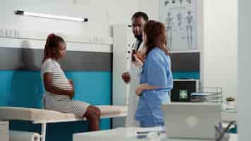 Foto grátis médico americano africano dando pílulas de prescrição para paciente grávida na visita de check-up. médico masculino ajudando mulher com barriga de gravidez, mostrando garrafa de tratamento medicamentoso.