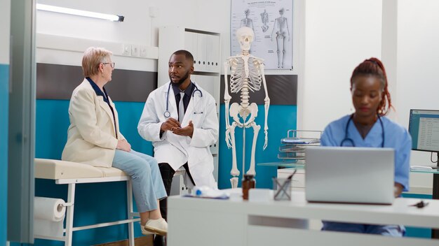 Médico americano africano fazendo consulta com mulher sênior no consultório médico, tendo consulta de check-up. Médico consultando paciente com doença na visita de exame de saúde.