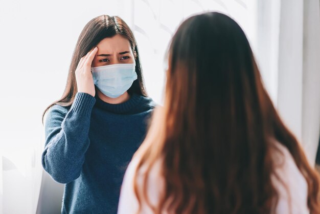 Médico asiático visita e examina uma jovem adulta no hospital com dor de cabeça o médico verificando e consultando cuidados de saúde usando uma máscara para proteger a pandemia covid19