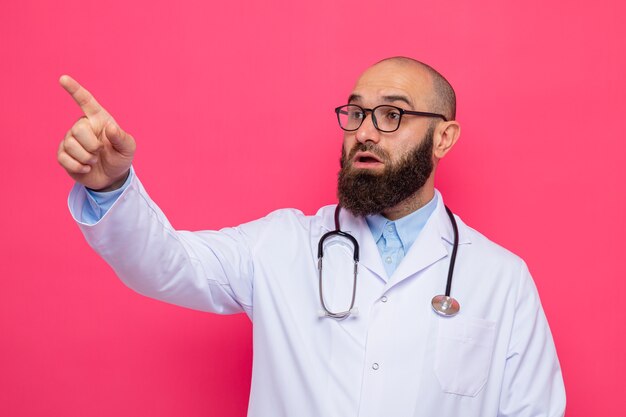 Médico barbudo com jaleco branco com estetoscópio no pescoço e óculos, olhando de lado, feliz e surpreso, apontando algo com o dedo indicador
