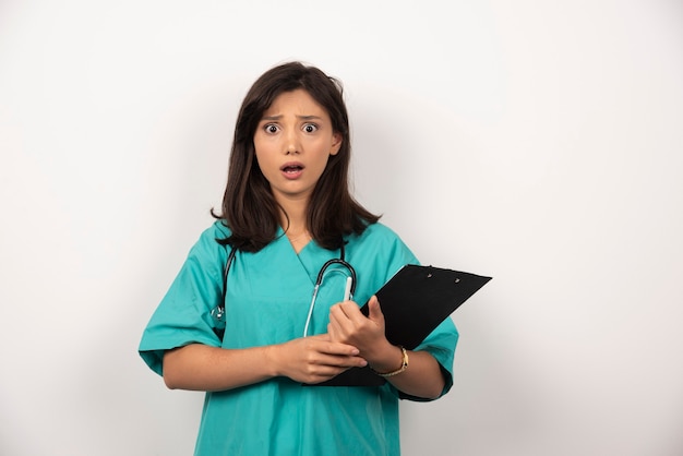 Médico chocado com estetoscópio segurando a prancheta em fundo branco. Foto de alta qualidade