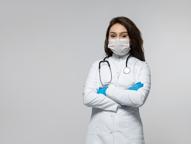 Médico com estetoscópio em uniforme médico branco, usando luvas azuis e máscara estéril branca