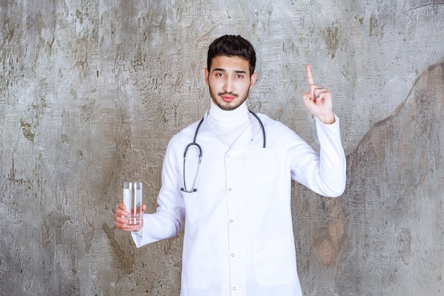 Médico com estetoscópio segurando um copo de água pura e pensando em algo.