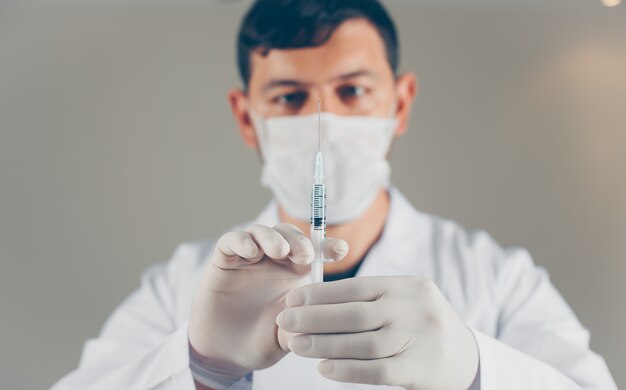 Médico com luvas segurando a seringa com as mãos, vista lateral.