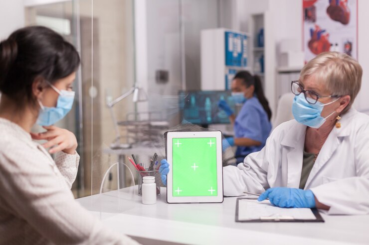 Foto grátis médico com máscara facial, olhando para o tablet com tela verde durante a consulta com paciente doente. enfermeira de uniforme azul.