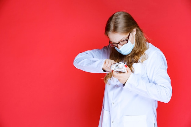 Foto grátis médico com máscara facial tentando acertar o despertador.