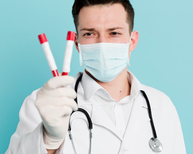 Foto grátis médico com máscara médica e estetoscópio segurando vacutainers