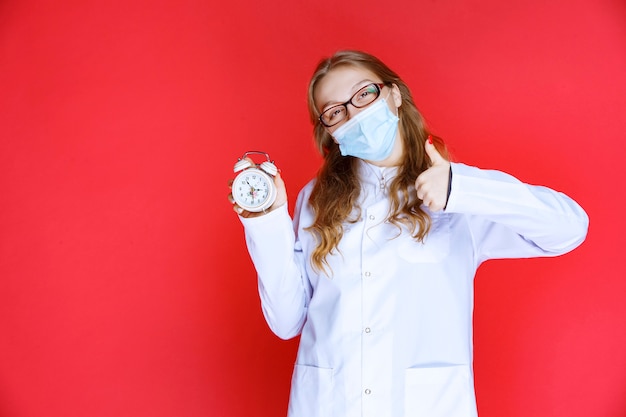 Foto grátis médico com máscara mostrando um relógio que indica a hora de tomar os medicamentos.