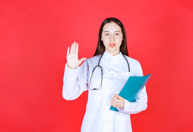 Médico com um estetoscópio segurando o histórico do paciente e levantando a mão para parar alguém.