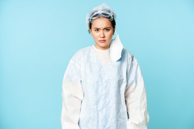 Médico de mulher asiática com raiva ou enfermeira usando equipamento de proteção pessoal, olhando com pele de desaprovação.