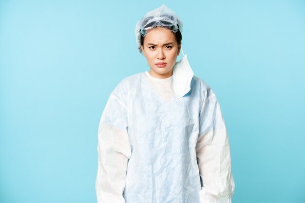 Médico de mulher asiática com raiva ou enfermeira usando equipamento de proteção pessoal, olhando com pele de desaprovação.