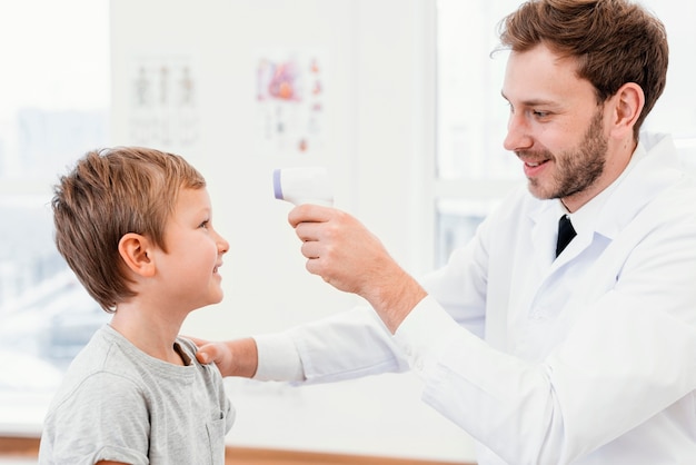 Médico de tiro médio verificando a temperatura da criança