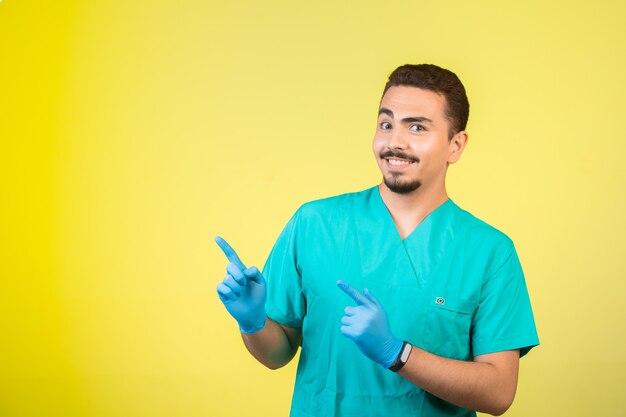 Médico de uniforme e máscara de mão apontando algo acima.