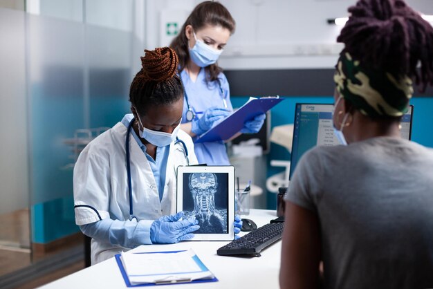 Foto grátis médico diagnosticando lesão na vértebra cervical, dor no pescoço, tomografia por raios-x no tablet para o paciente durante a consulta. médico usando luvas de proteção e máscara facial para exame médico em hospital estéril e limpo