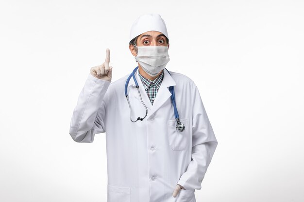 Médico do sexo masculino de frente para o terno branco com máscara devido a cobiçado na superfície branca
