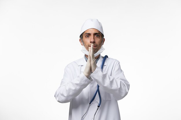 Médico do sexo masculino de frente para o terno e máscara devido a coronavírus usando luvas em uma mesa branca