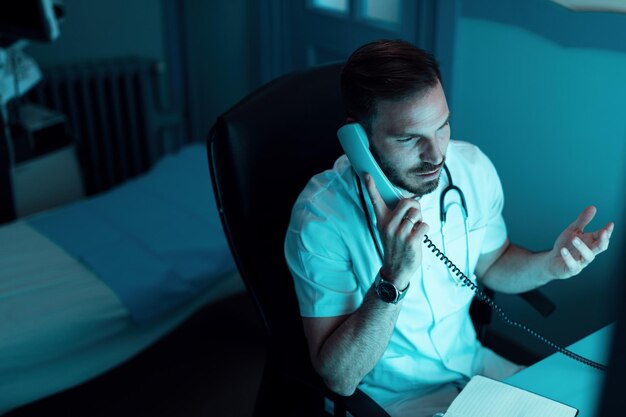 Médico do sexo masculino sentado no hospital e conversando com alguém por telefone