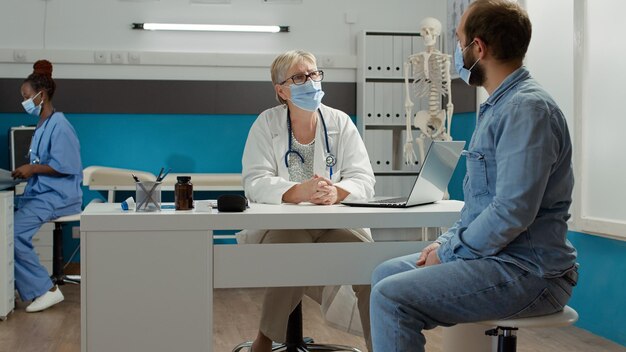 Médico e paciente do sexo masculino conversando no exame médico no gabinete. Fazer consulta de saúde na consulta de check-up para dar suporte e prescrição de medicamentos durante a pandemia.