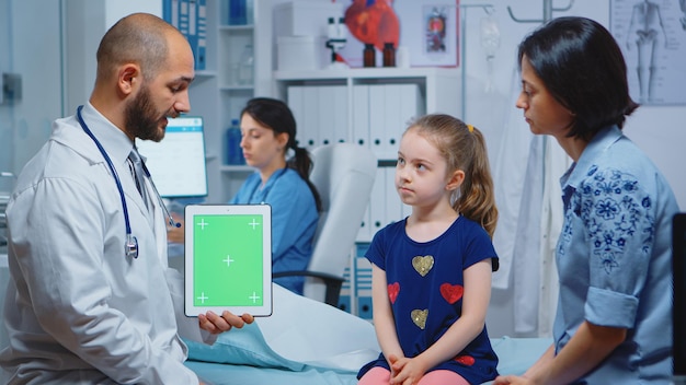 Médico e pacientes olhando para tablet de tela verde no consultório médico. Especialista em saúde com tela de substituição de maquete isolada de notebook de chroma key. Tema médico relacionado à medicina de keying fácil.