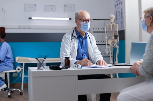 Médico escrevendo em arquivos da área de transferência enquanto consulta a mulher durante a pandemia de covid 19. Médico com máscara facial preparando documento de prescrição para tratamento contra doenças.