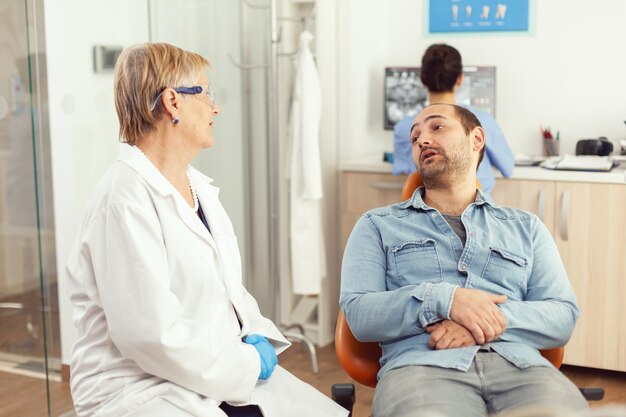 Médico estomatologista sênior discutindo com o paciente antes de examinar a saúde bucal enquanto está sentado no consultório de estomatologia do hospital