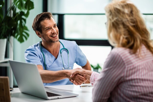 Médico feliz apertando as mãos da esposa de seu paciente sênior na clínica médica