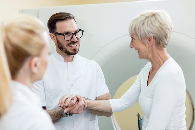 Médico feliz se comunicando com paciente do sexo feminino e apoiando-a antes do exame de tomografia computadorizada no hospital