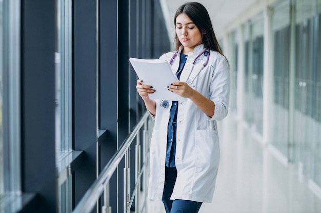 Médico feminino atraente em pé com documentos no hospital