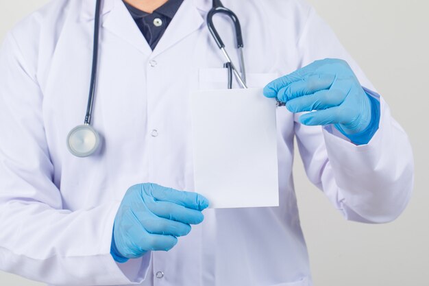 Médico homem segurando o cartão de papel em branco no jaleco branco e luvas
