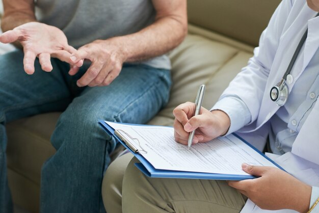 Médico irreconhecível, conversando com o paciente em casa e fazendo anotações