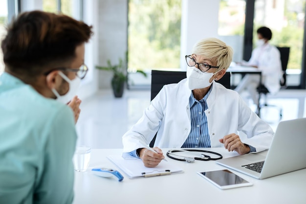 Médico maduro usando máscara facial enquanto conversa com um paciente na clínica médica
