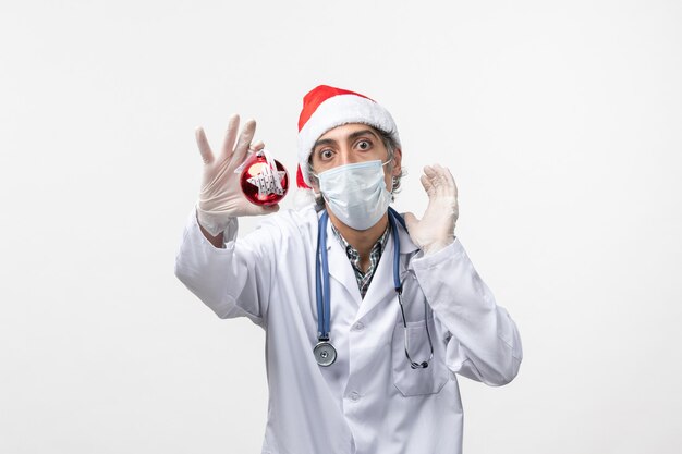Médico masculino com máscara e brinquedo na parede branca saúde cobiça vírus de ano novo