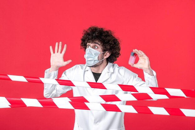 Médico masculino de vista frontal em uniforme médico segurando frascos na cor de fundo vermelho covid-curar alerta de perigo para a saúde quarentena de isolamento