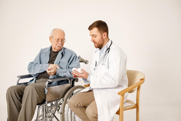 Médico masculino e ancião em cadeira de rodas isolado em um fundo branco