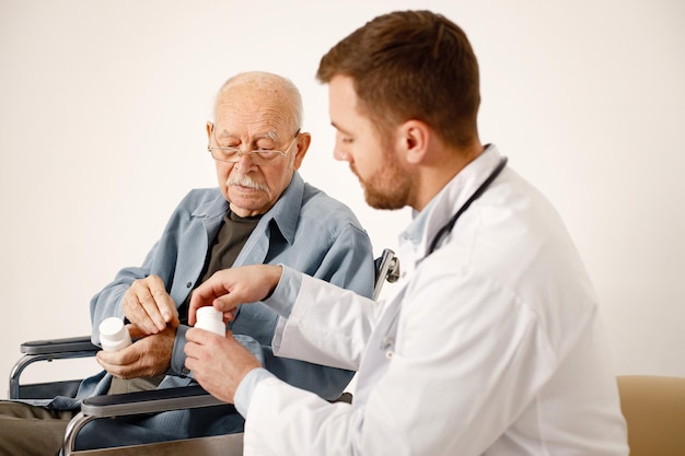 Médico masculino e ancião em cadeira de rodas isolado em um fundo branco