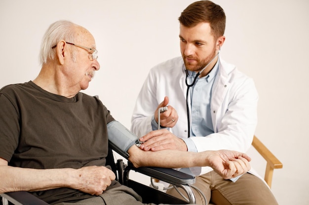 Médico masculino e ancião em cadeira de rodas isolado em um fundo branco