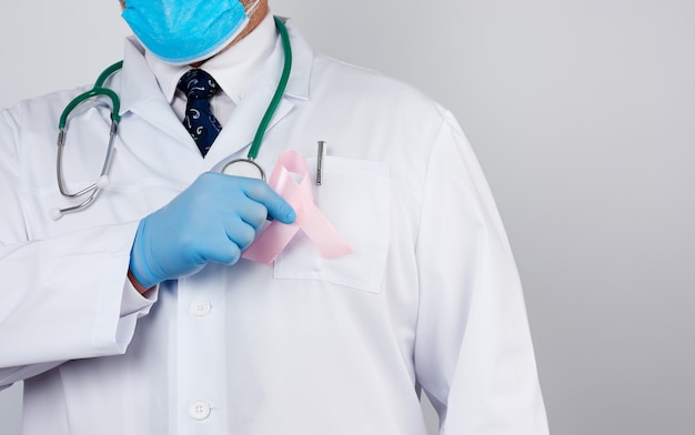Médico masculino em um jaleco branco e gravata fica e segura uma fita de seda rosa na forma de um laço