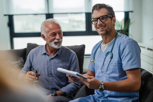 Médico masculino feliz visitando pacientes idosos em casa e passando por documentos médicos