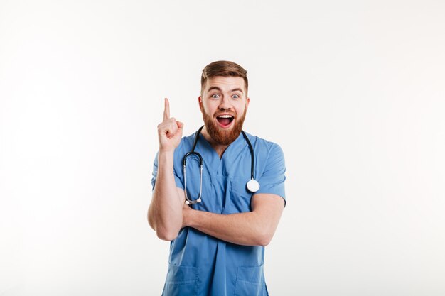 Médico masculino jovem animado apontando o dedo para cima na copyspace