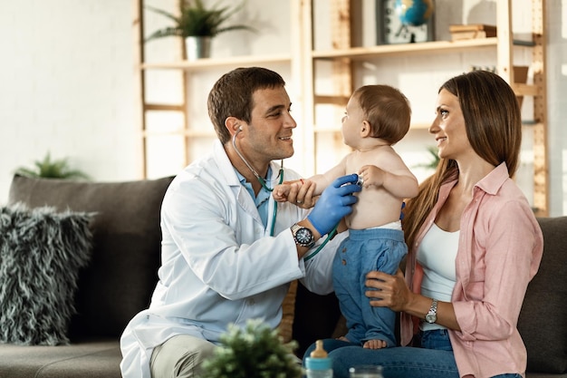 Médico masculino sorridente usando estetoscópio e verificando a frequência cardíaca do menino durante a consulta médica