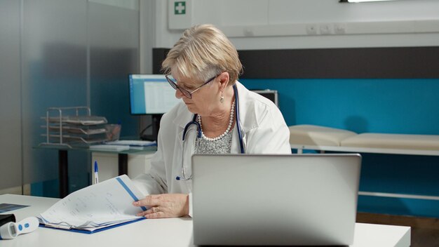 Médico que planeja o exame de visita de check-up no laptop, usando o sistema de saúde para trabalhar na hora marcada. Médico analisando informações sobre doenças para dar suporte e ajuda na consulta.