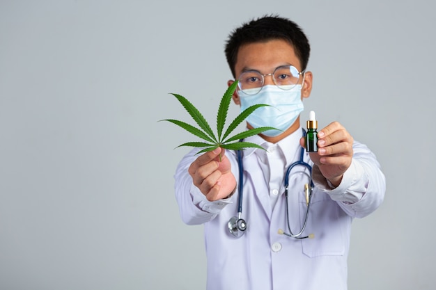 Foto grátis médico segurando a folha de cannabis e uma garrafa de óleo de cannabis na parede branca.