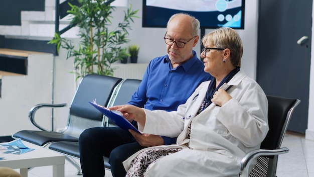 Foto grátis médico sentado em uma cadeira no lobby do hospital, explicando o diagnóstico da doença a um paciente idoso discutindo o tratamento de cuidados de saúde. homem doente fazendo uma consulta de visita de check-up, recebendo suporte de medicamentos