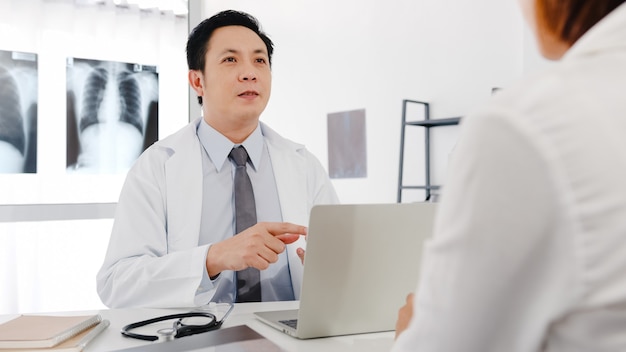 Médico sério da Ásia em uniforme médico branco usando computador laptop está dando uma ótima palestra.